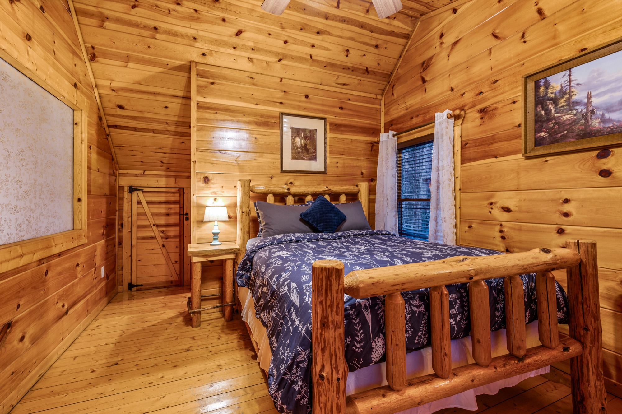 Bearadise bedroom with a vaulted ceiling, log bed frame, and navy floral bedding
